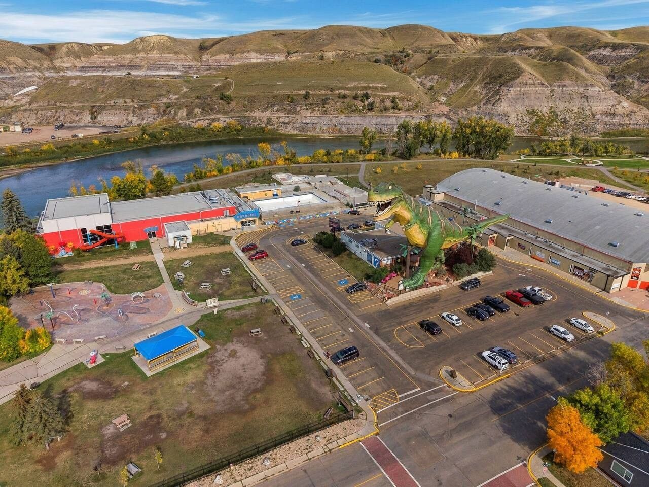 An aerial view of a commercial area with parking lots, a large building with a green roof, and a river in the background.
