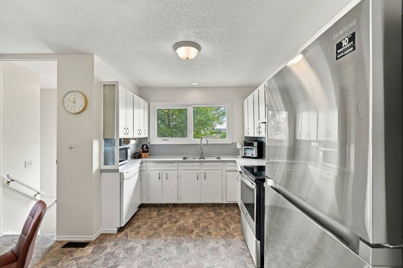 A modern kitchen with white cabinets, a stainless steel refrigerator, a microwave, and a window providing natural light.