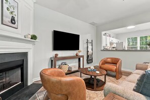 Un salon moderne avec une cheminée, des fauteuils en cuir, une table basse et un téléviseur à écran plat.