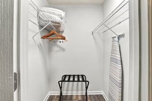 Ein begehbarer Kleiderschrank mit Metallregalen, einem hölzernen Kleiderbügel und einem schwarzen Wäscheständer aus Metall.