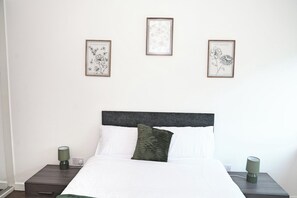 Een slaapkamer met een bed, twee nachtkastjes en drie ingelijste botanische afbeeldingen aan de muur.