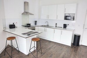 A modern kitchen with white cabinetry, a stainless steel range hood, a microwave, and two stools at the island. - Cozy Croydon Apartment Retreat (Croydon)