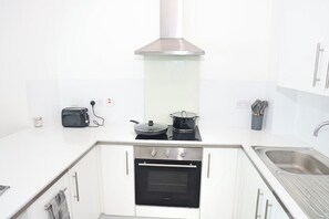 Een moderne keuken met witte kastjes, een roestvrijstalen spoelbak, een ingebouwde oven en een afzuigkap.