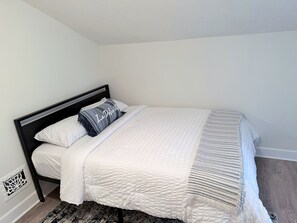 Una cama individual con un edredón blanco acolchado y una manta de rayas grises y blancas.