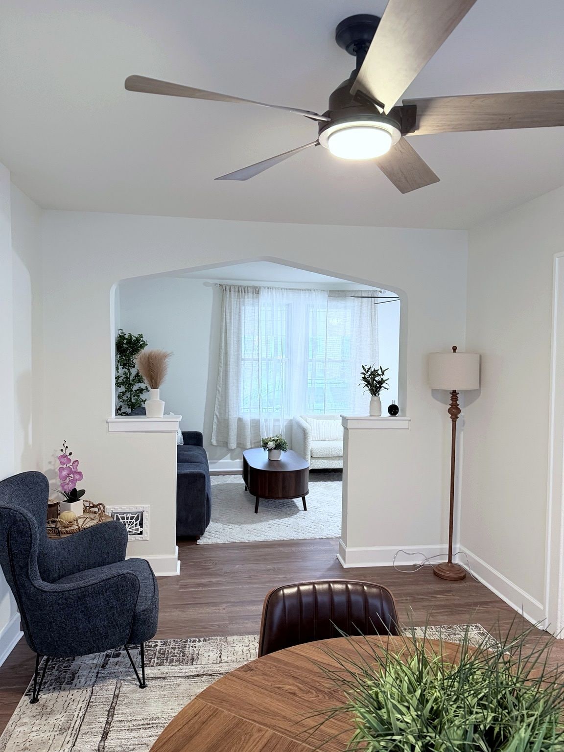 Un salon moderne avec un ventilateur de plafond, une table à manger avec des chaises, un canapé et une table d’appoint agrémentée d’objets décoratifs.