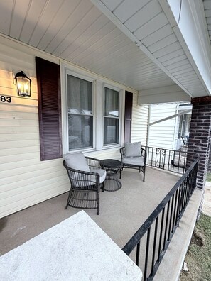 A covered porch with a table and chairs, a brick wall, and a window with shutters.
