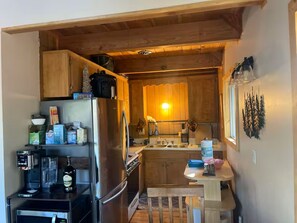 Een functionele keuken met houten kastjes, een koelkast, een koffiezetapparaat en een kleine eettafel.