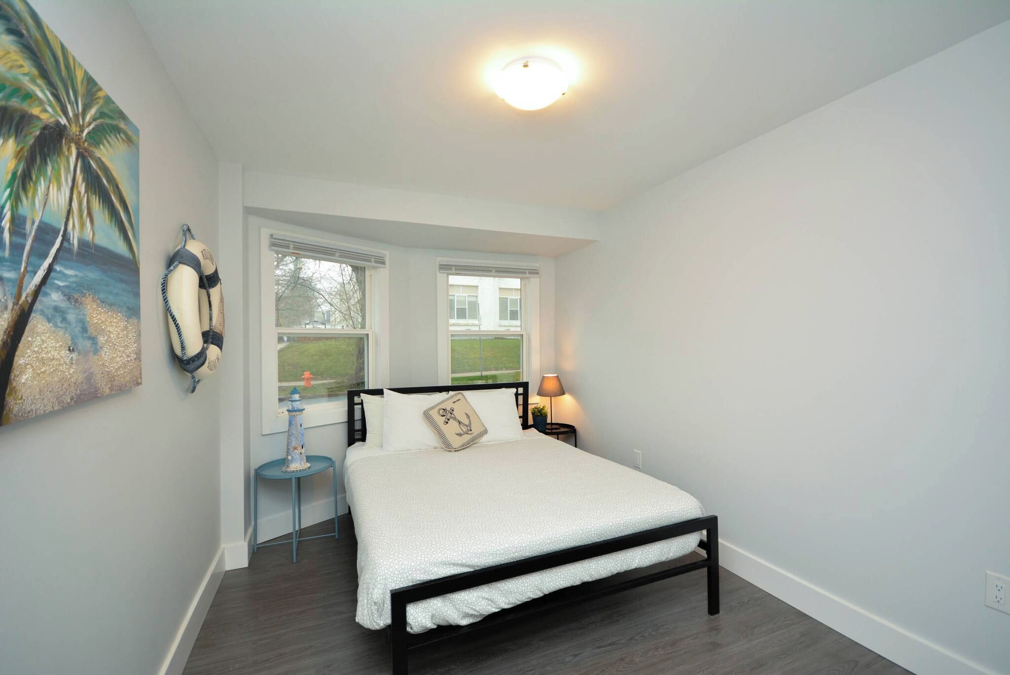 A bedroom with a bed, a nightstand, a lamp, a window, and a painting.
