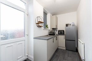 A compact kitchen with white cabinets, a built-in oven, a refrigerator, and a window with a view. - The Cosy Pavilion Stylish 2BR Home With Free Street Parking (Durham)