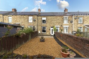 Une maison en pierre à deux étages, avec une allée en gravier et un petit jardin agrémenté de plantes en pot.