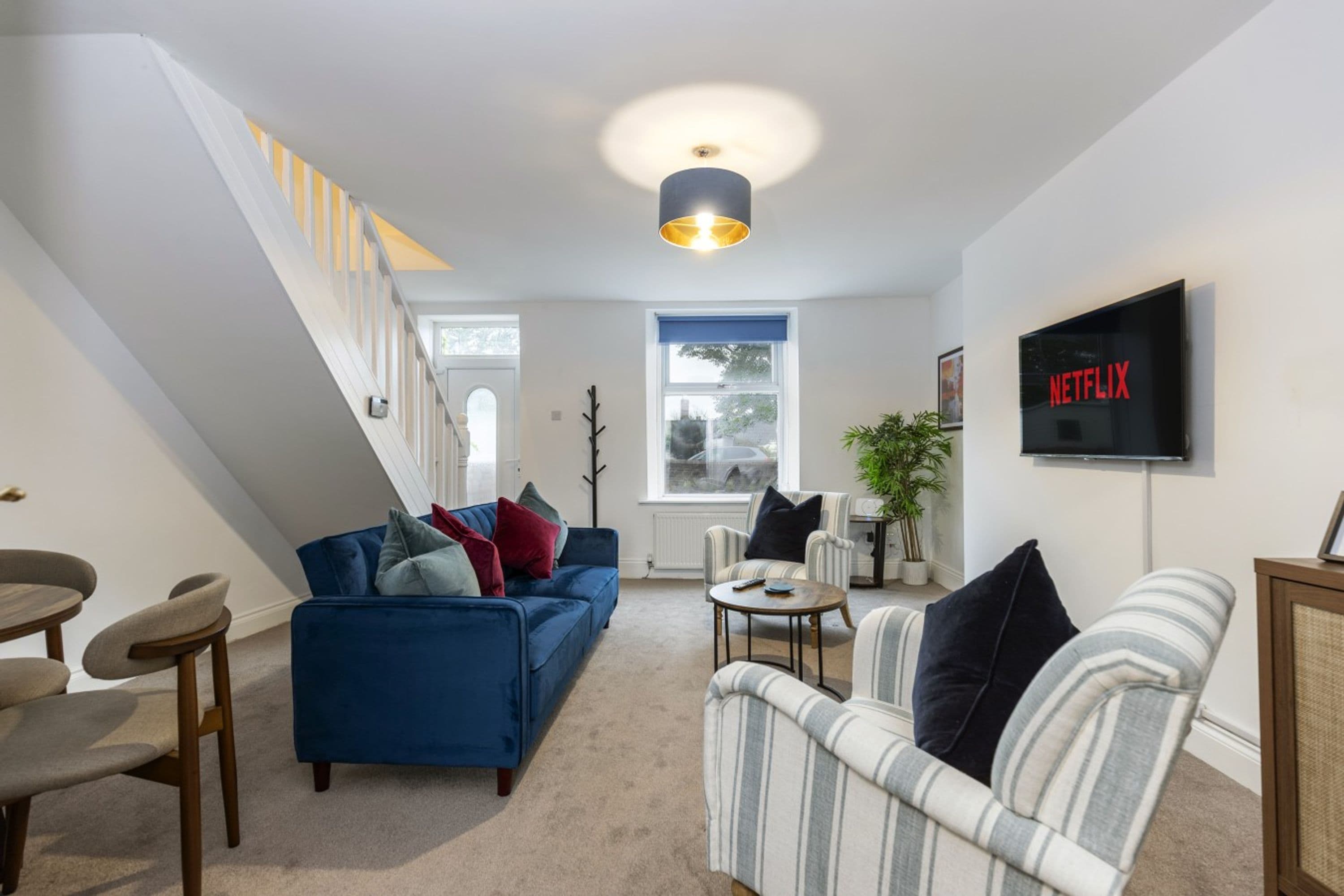 Een moderne woonkamer met een blauwe bank, een gestreept fauteuil en een aan de muur bevestigde televisie.