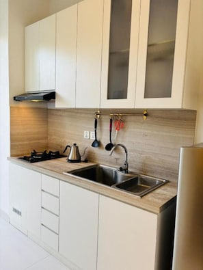 A modern kitchen with white cabinets, a stainless steel sink, and a gas stove. - The Renon Residence (Denpasar)