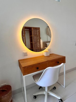 A wooden desk with a round mirror, a white chair, and a small white table with a tissue box. - The Renon Residence (Denpasar)