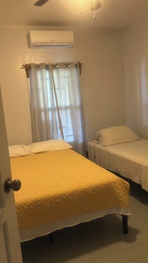 A room with a bed, a bedside table, a window with curtains, and an air conditioning unit on the wall. - Tranquil 2-bedroom apartment with AC in charming Pensacola (Roatan)