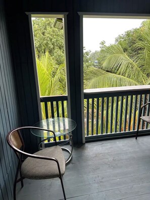 A balcony with a glass table and two chairs, overlooking a lush green landscape. - Tranquil 2-bedroom apartment with AC in charming Pensacola (Roatan)