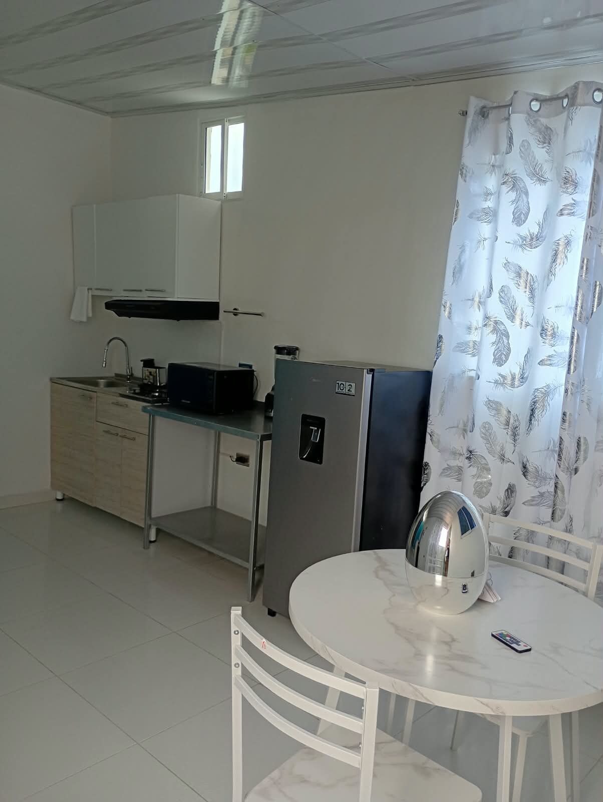 A compact kitchen with a refrigerator, a microwave, and a sink. There is a dining table with chairs and a decorative item on it.