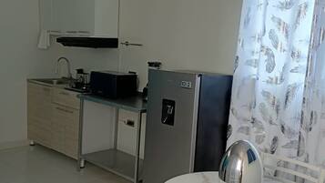 A compact kitchen with a refrigerator, a microwave, and a sink. There is a dining table with chairs and a decorative item on it.