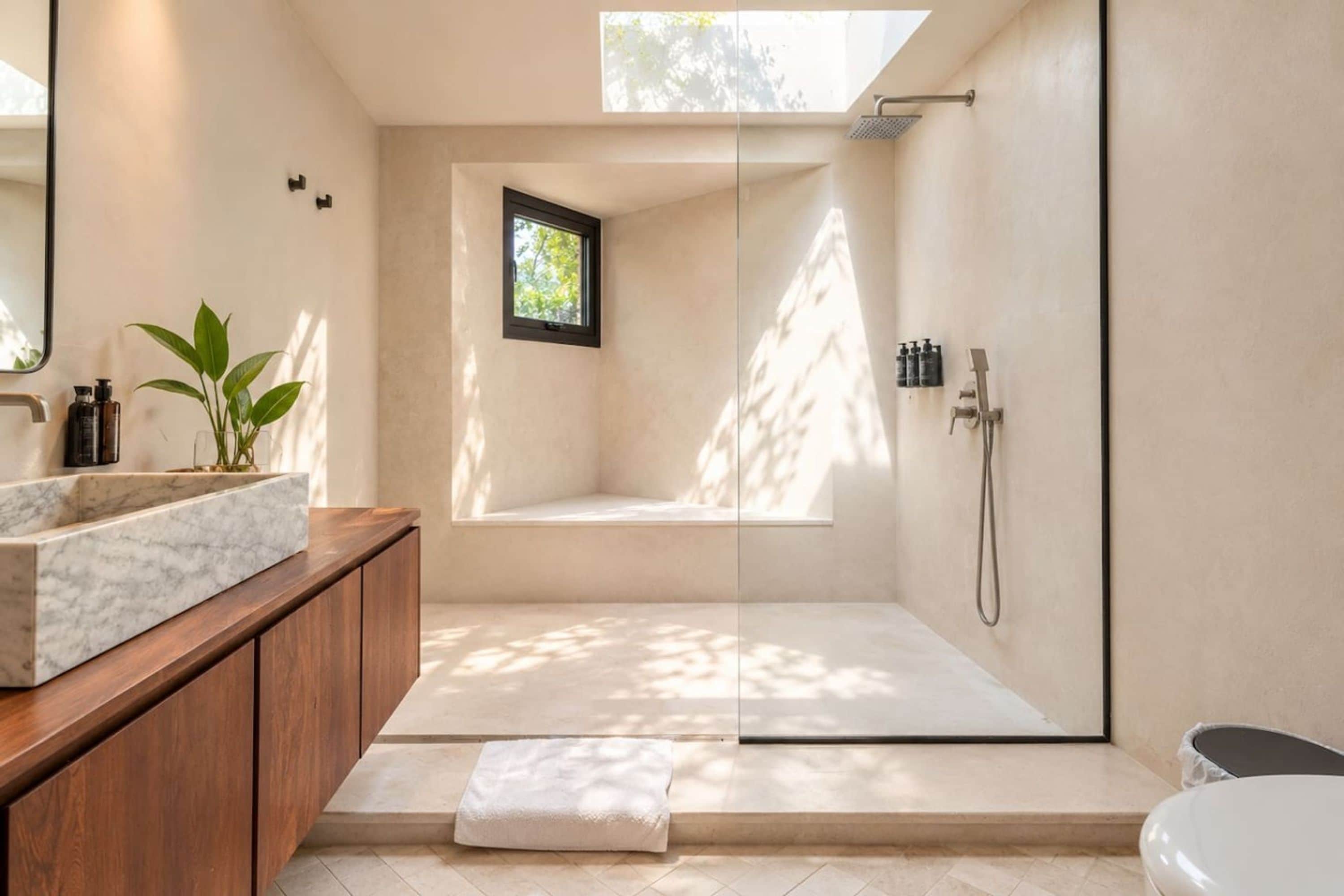 A modern bathroom with a marble sink, a wooden vanity, a glass-enclosed shower, and a small window.