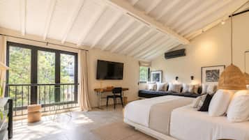 A bedroom with a large bed, a desk, a chair, a TV, and a balcony with a view of trees.