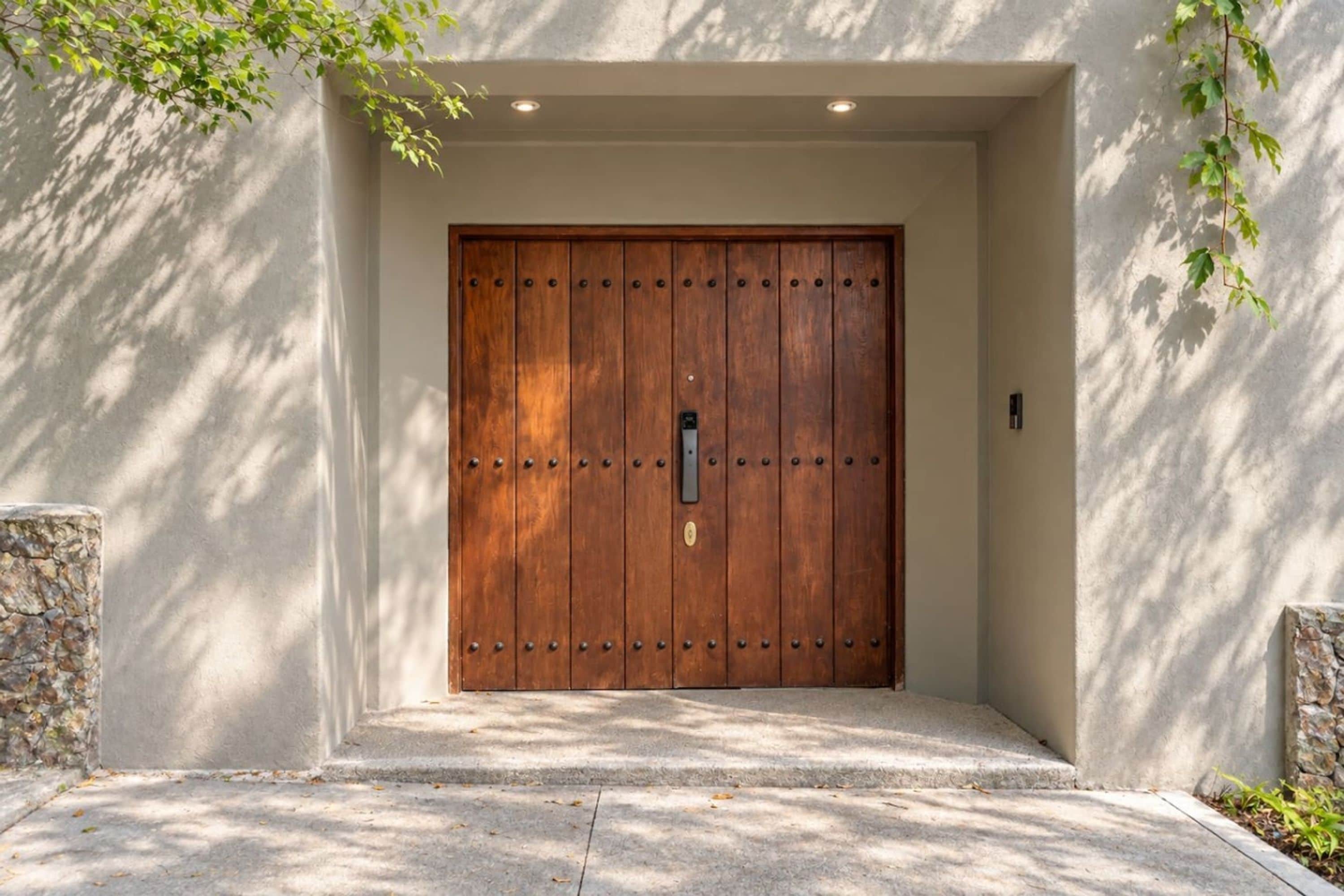 Una puerta de madera con un ojo de cerradura y una pequeña placa, ubicada en un acceso de hormigón con detalles de piedra a ambos lados.