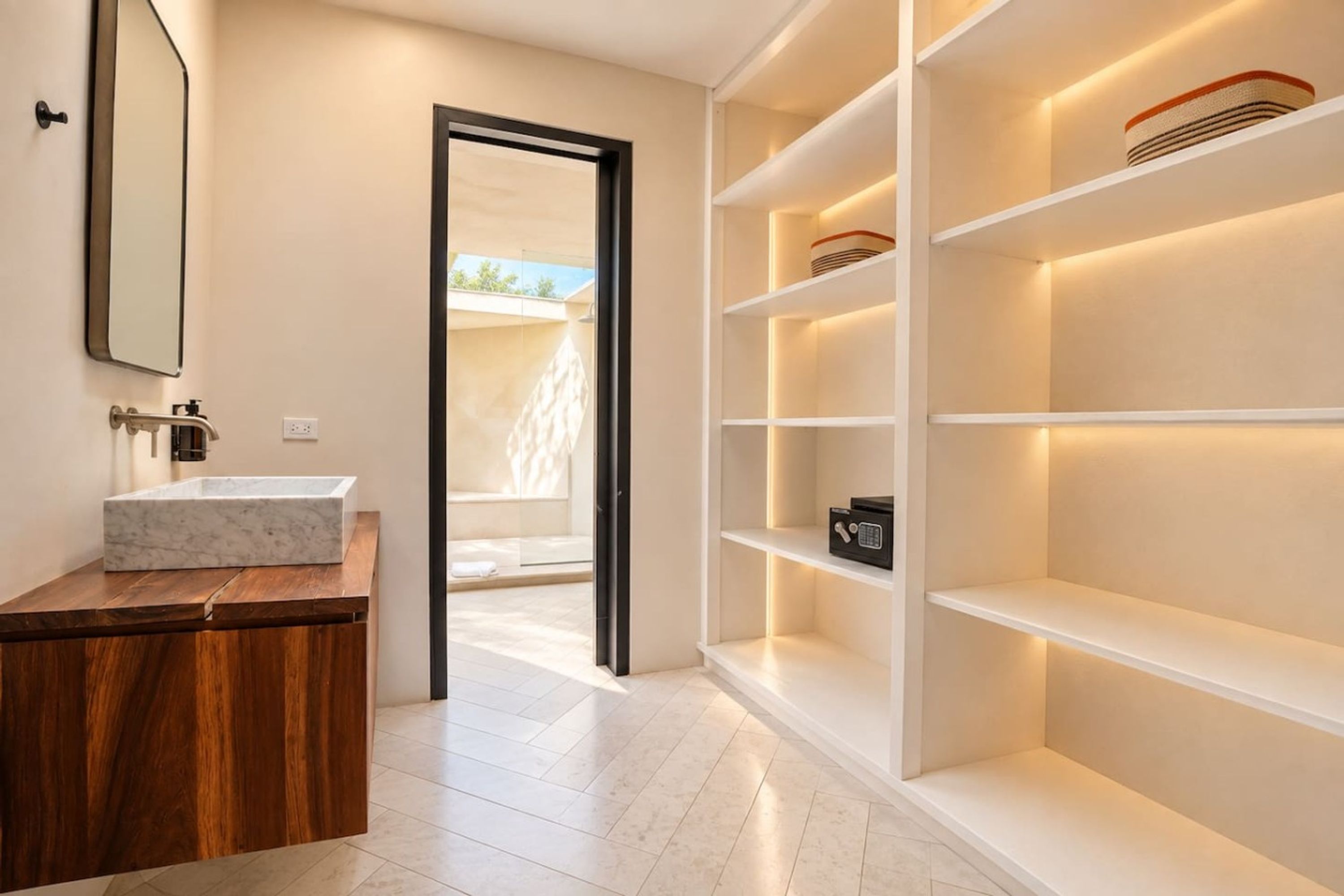 A modern bathroom with a marble sink, wooden vanity, and built-in shelves with a safe.