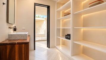 A modern bathroom with a marble sink, wooden vanity, and built-in shelves with a safe.