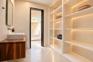 Un baño moderno con lavamanos de mármol, tocador de madera y estantes empotrados con una caja fuerte.