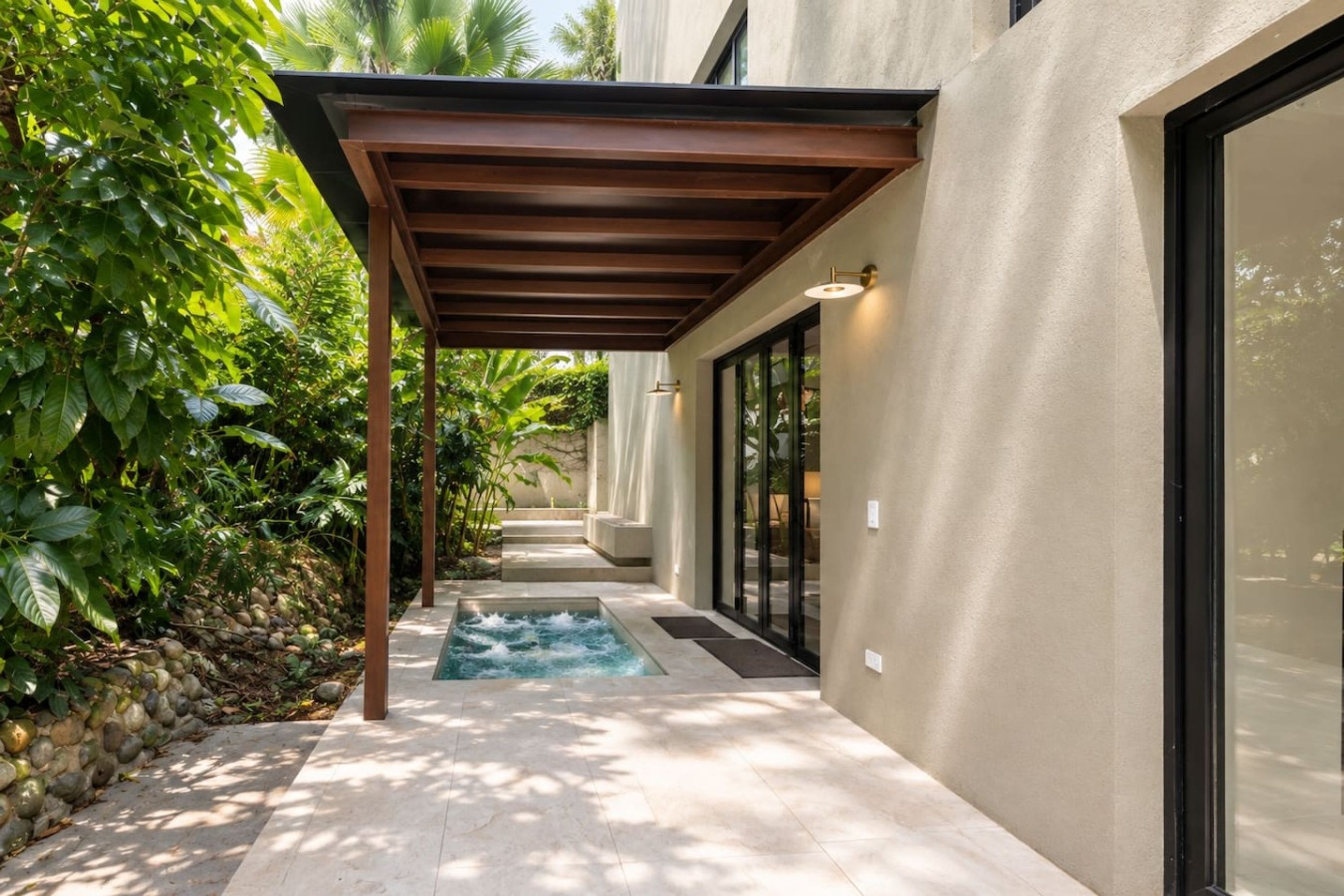 A modern building with a covered outdoor area, a small water feature, and lush greenery.