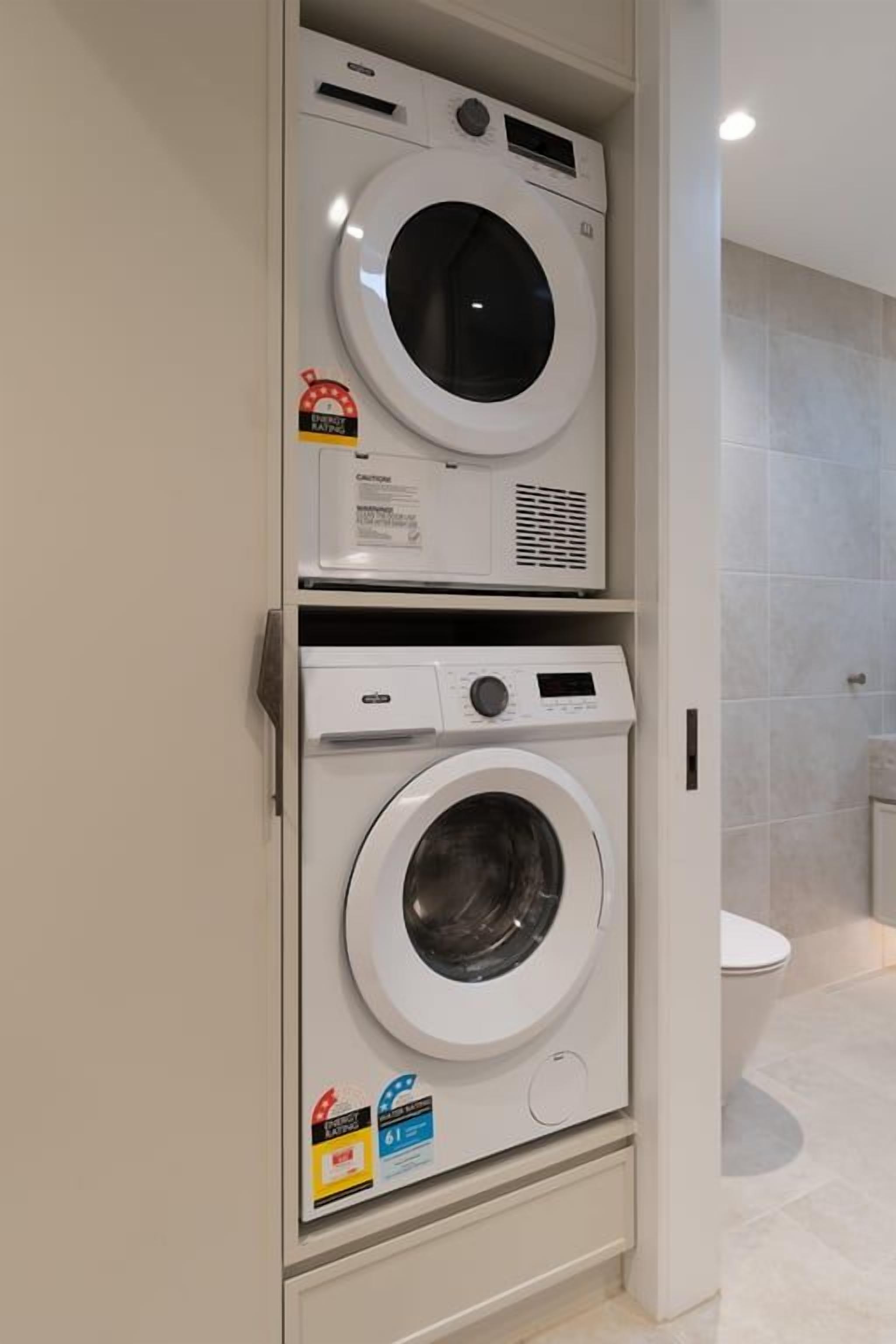 A laundry room with two stacked washing machines, a toilet, and a tiled wall.