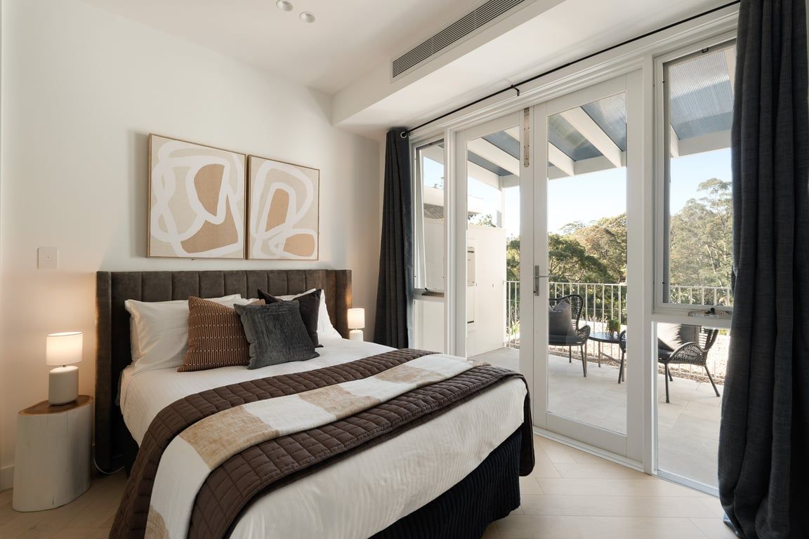 A bedroom with a large bed, a view of the outdoors through a sliding glass door, and artwork on the wall.