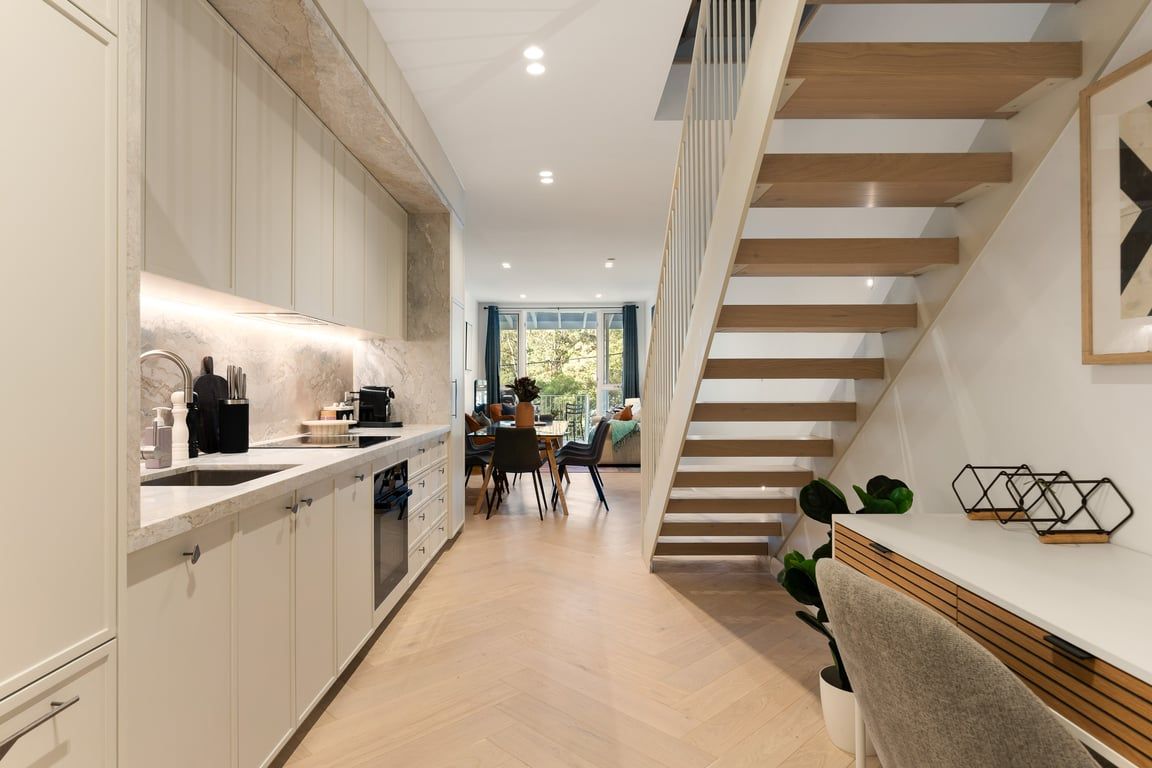 A modern kitchen with a dining area, wooden staircase, and a view to the outdoors.
