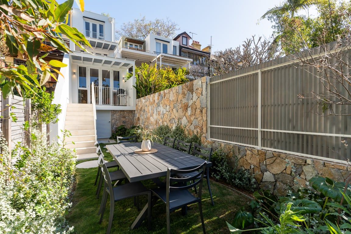A residential backyard with a stone wall, a wooden fence, and a dining table with chairs.