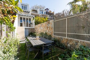 A residential backyard with a stone wall, a wooden fence, and a dining table with chairs. - Ivyhurst - Fully Renovated Paddington Terrace (Woollahra)