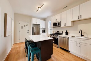 A modern kitchen with white cabinetry, stainless steel appliances, and a central island with stools. - The Grandstand - Modern 4Br 3Ba Penthouse near Sox Stadium (Chicago)