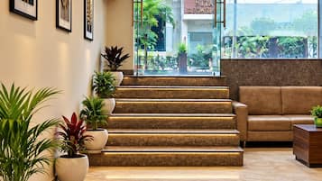 Um saguão de hotel com uma escada que leva ao Portão Leste, plantas em vasos, um sofá de couro e obras de arte emolduradas nas paredes.