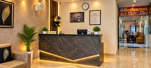 A reception desk with a marble top, a clock, framed artwork, and a sign for a restaurant. - Hotel Sulit Agra Near Taj Mahal  (Agra)