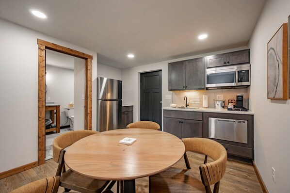 A modern kitchen with stainless steel appliances, a round wooden table, and dark cabinetry.
