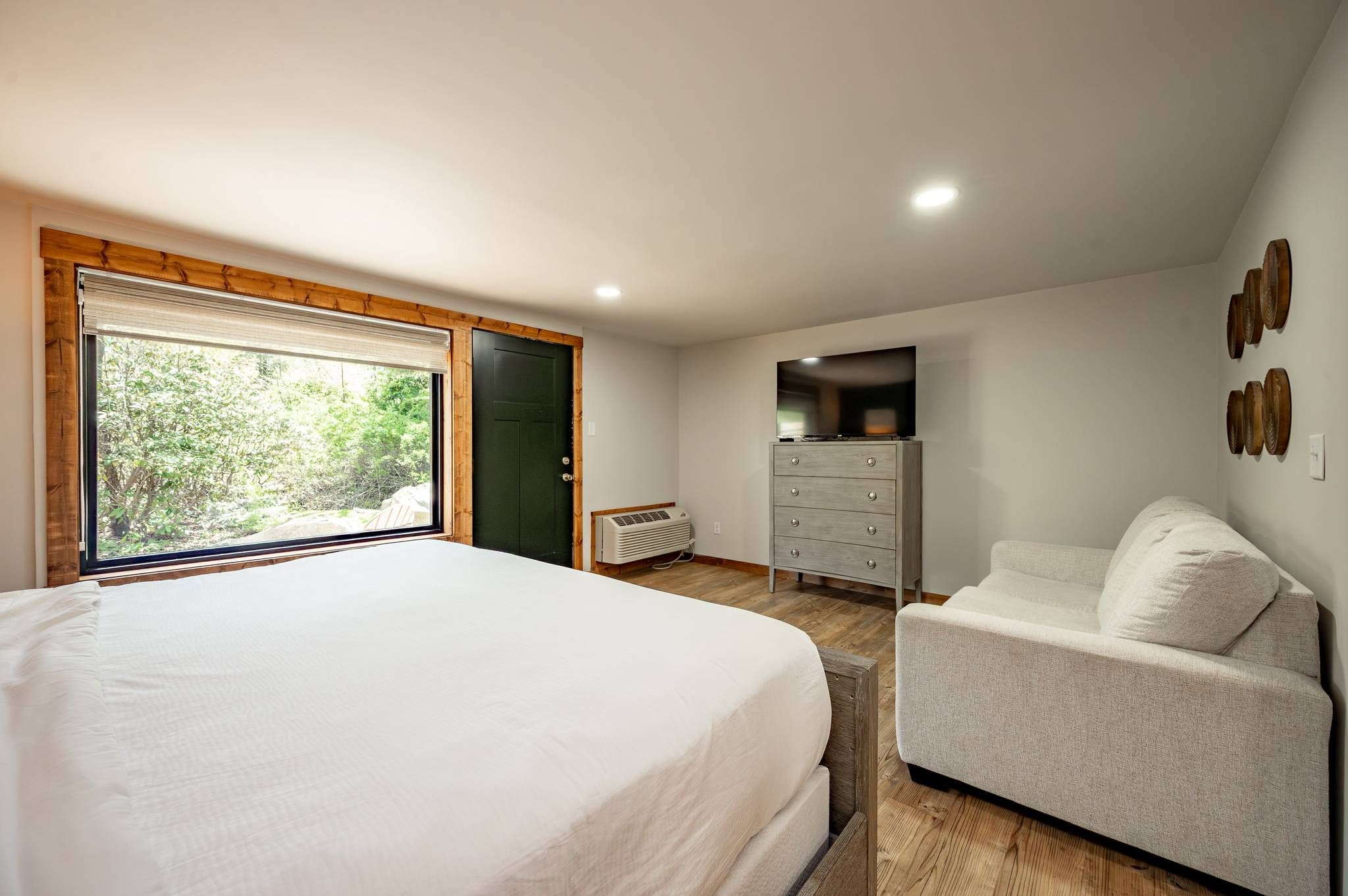 Quarto com cama grande, penteadeira, televisão e vista para o verde lá fora.
