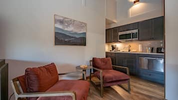 Un espacio habitable compacto con kitchenette, dos sillones de cuero, una mesita redonda y un cuadro de un paisaje montañoso.