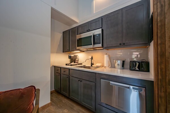 A compact kitchen with dark cabinets, a stainless steel dishwasher, a microwave, and a toaster.