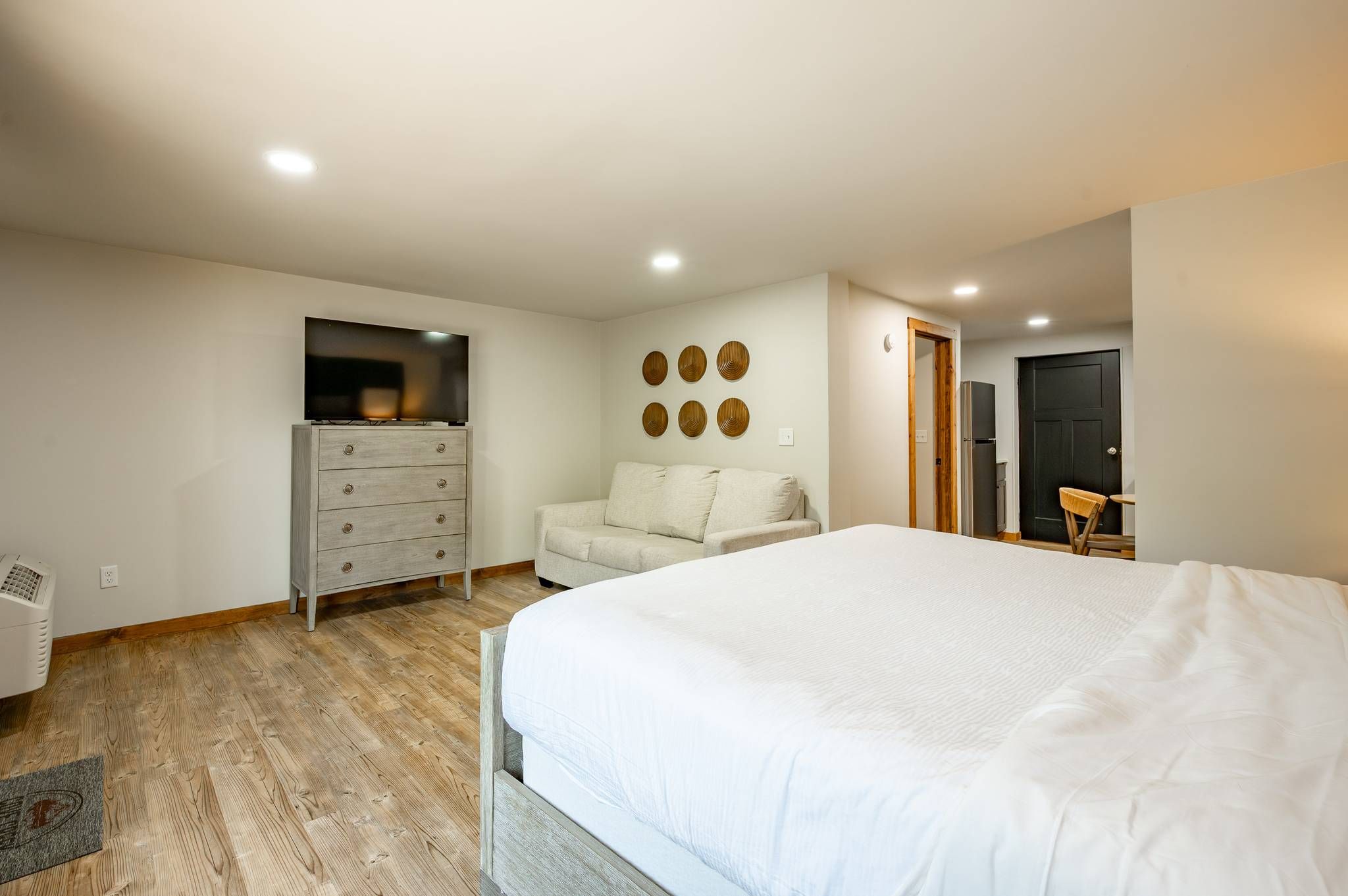 Une chambre à coucher avec un lit, une commode, une chaise, un téléviseur et une porte.