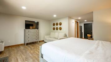 Une chambre à coucher avec un lit, une commode, une chaise, un téléviseur et une porte.