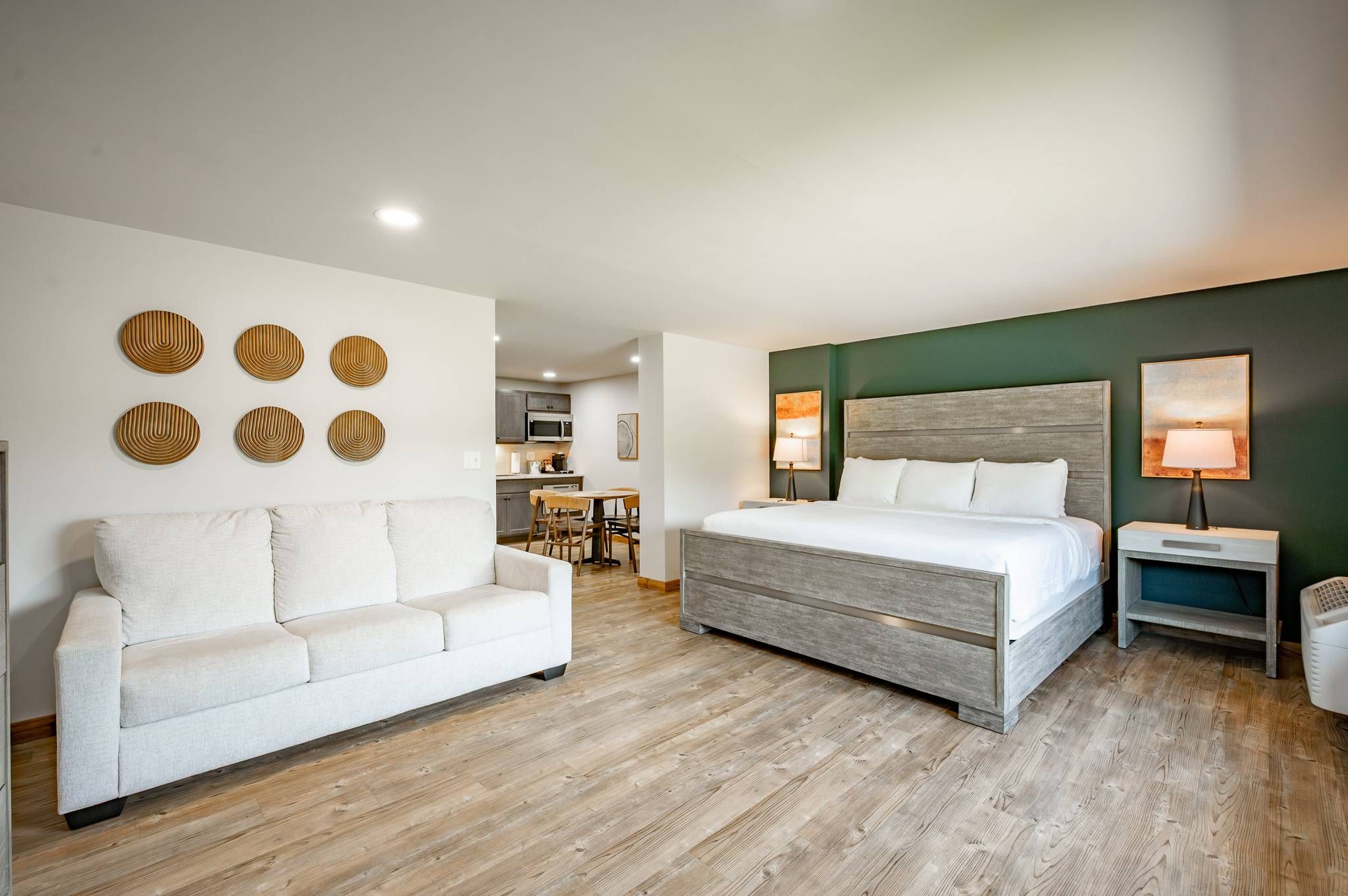 A hotel room with a bed, a sofa, a bedside table, a lamp, and a wall with circular wall art.