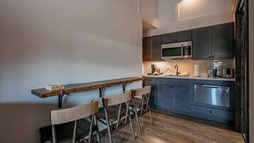 A modern kitchen with a wooden bar counter and stools, stainless steel appliances, and a light fixture above the counter.