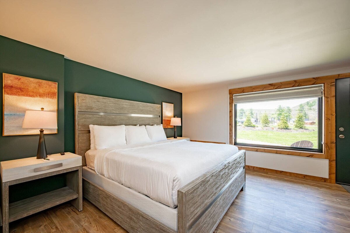 A neatly arranged bedroom with a bed, bedside tables, and a window offering a view of the outdoors.