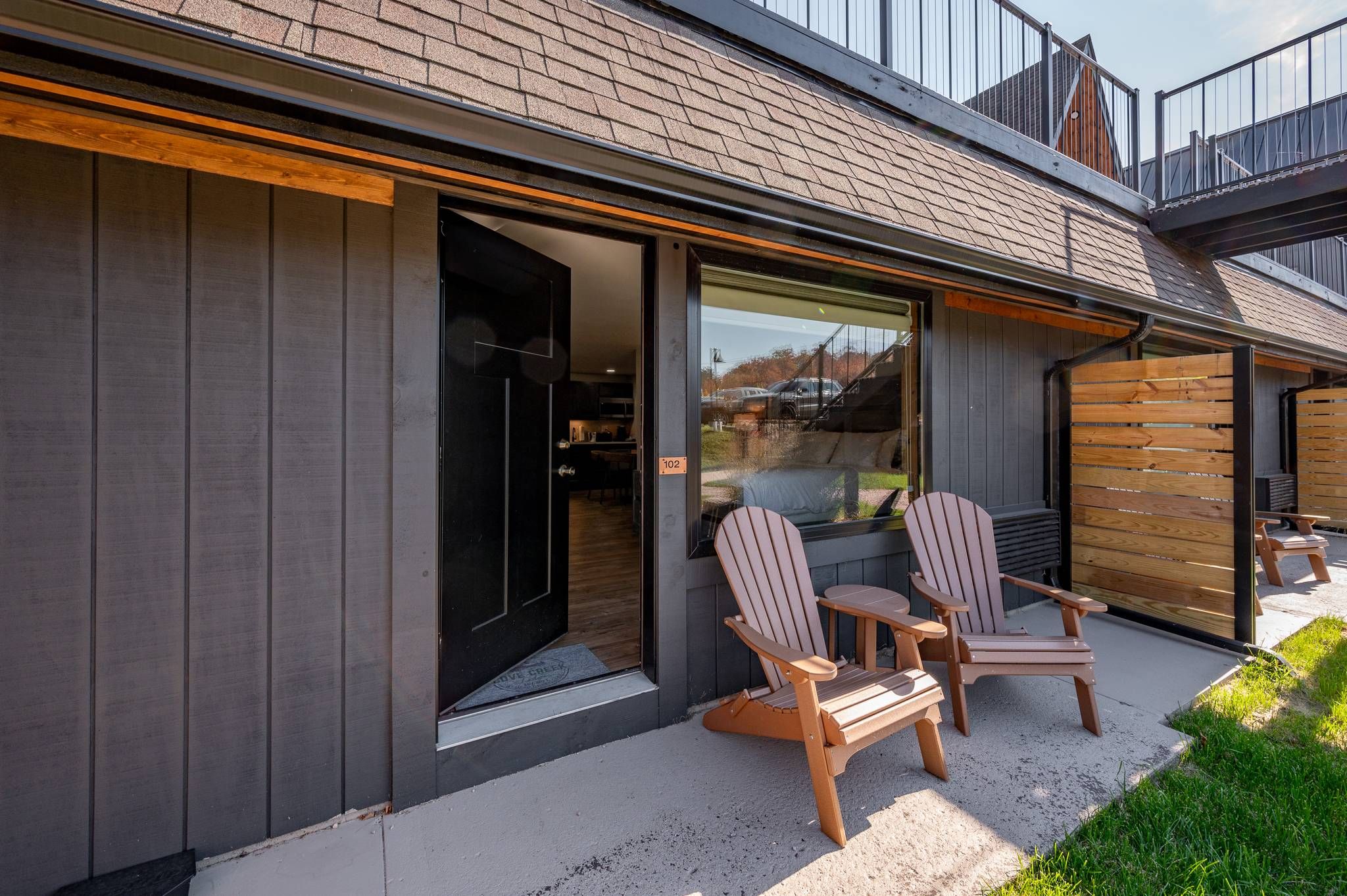 Une maison moderne dotée d’une grande porte-fenêtre coulissante qui donne sur une terrasse. On y trouve deux fauteuils Adirondack.