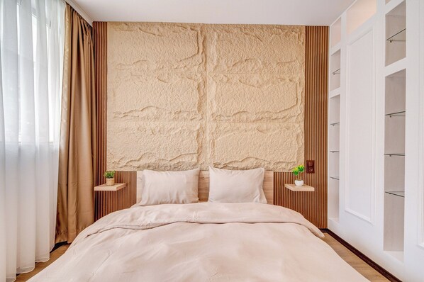 Un dormitorio con una cama grande, dos mesitas de noche con lámparas, una pared texturizada y una ventana con persianas.