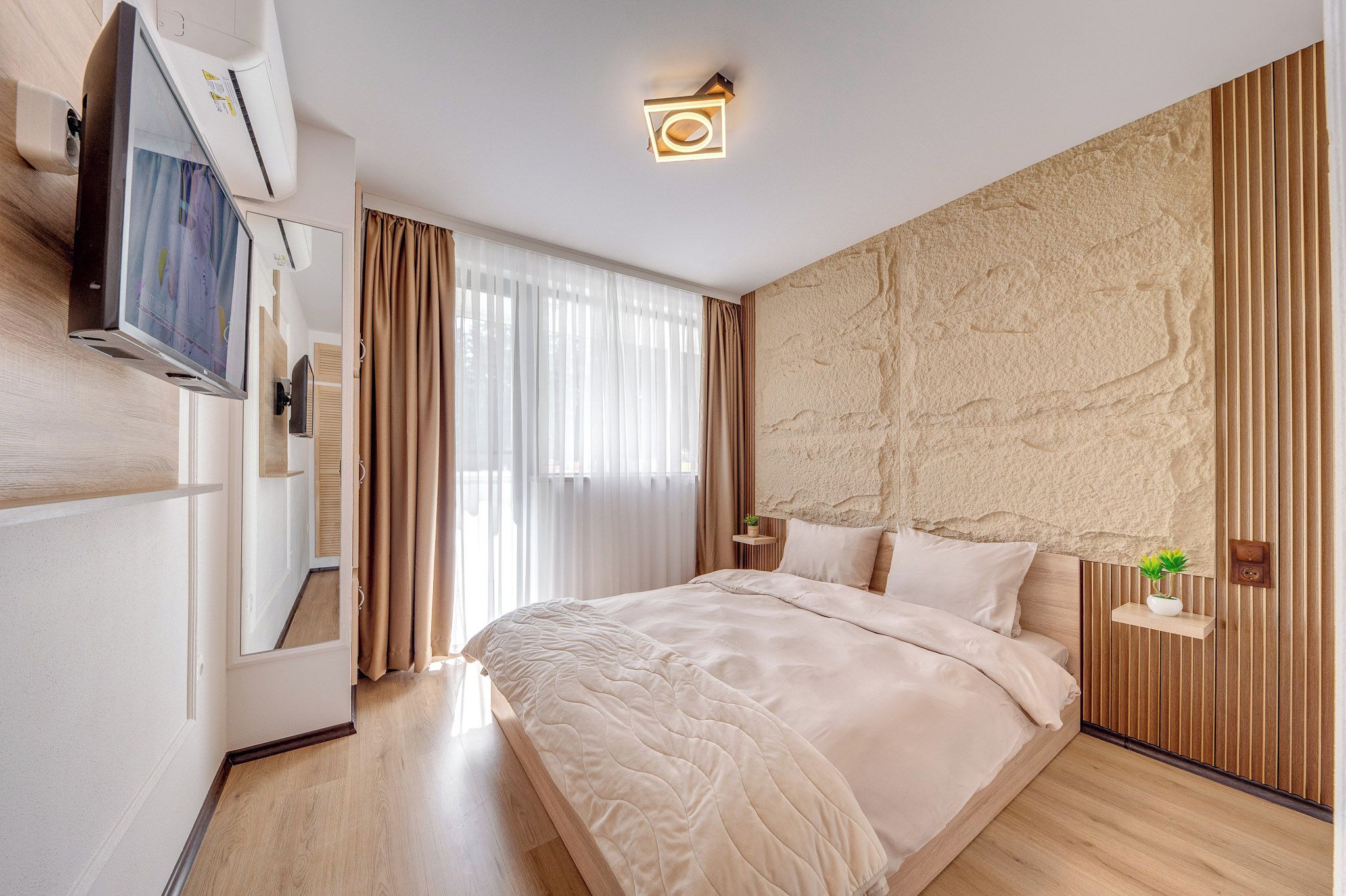 A hotel room with a bed, a TV, a desk, and a window with curtains.