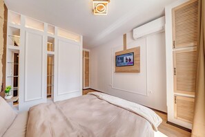 Un dormitorio con cama, televisor montado en la pared, equipo de aire acondicionado y armario de madera con puertas persianas.