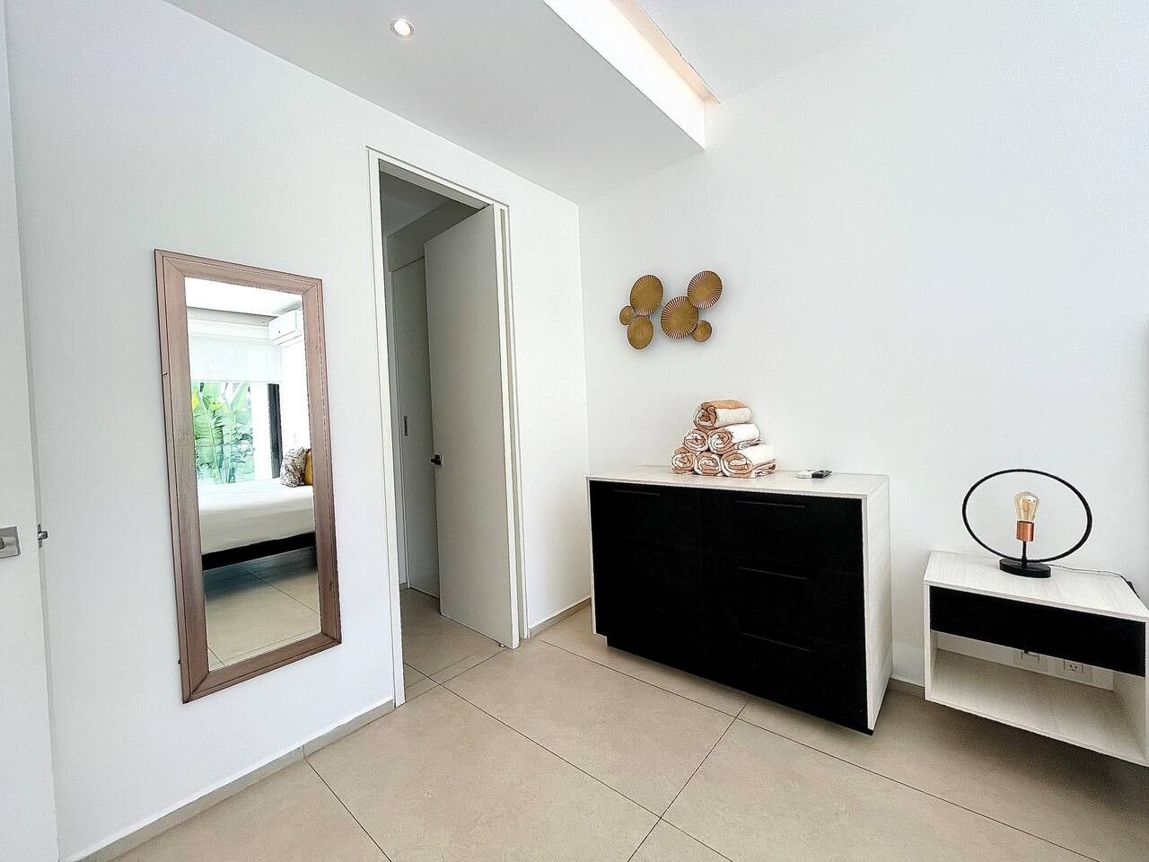 Une chambre moderne avec un grand miroir, une commode noire et blanche et un luminaire fixé au mur.